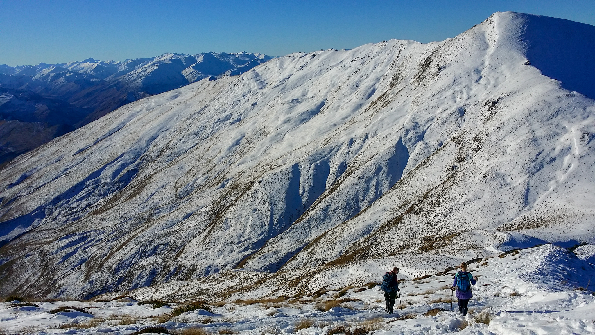 Two hikers walking in snow during winter with Bowen Peak in the background