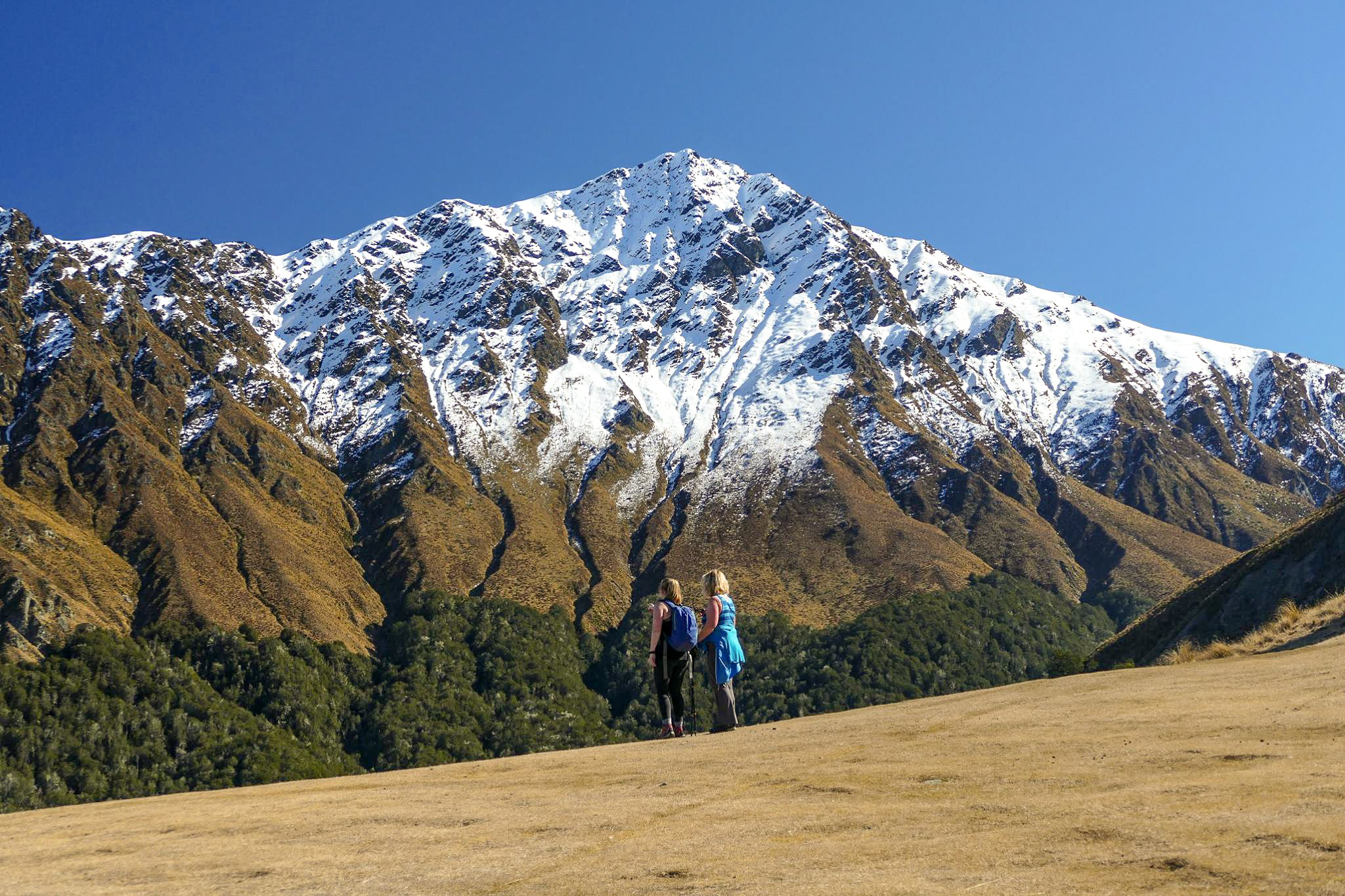 Two female hikers standing at the top of Bob's Peak looking at a snowy Ben Lomond summit