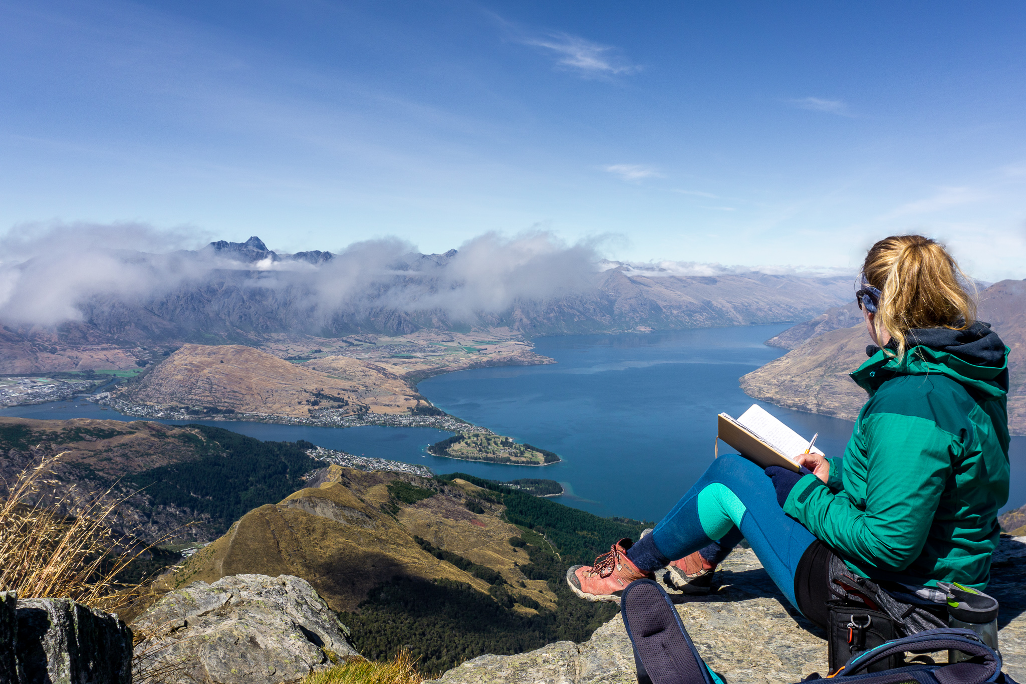 Female hiker writing in her diary at the top of Ben Lomond with Lake Wakatipu in the background