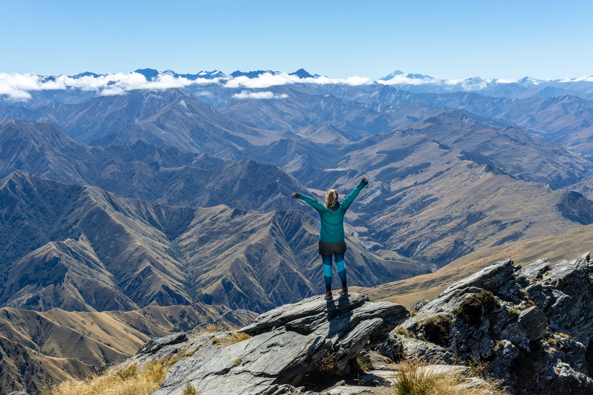 Female hiker standing with arms raised, with the Southern Alps and Mt Aspiring in the background