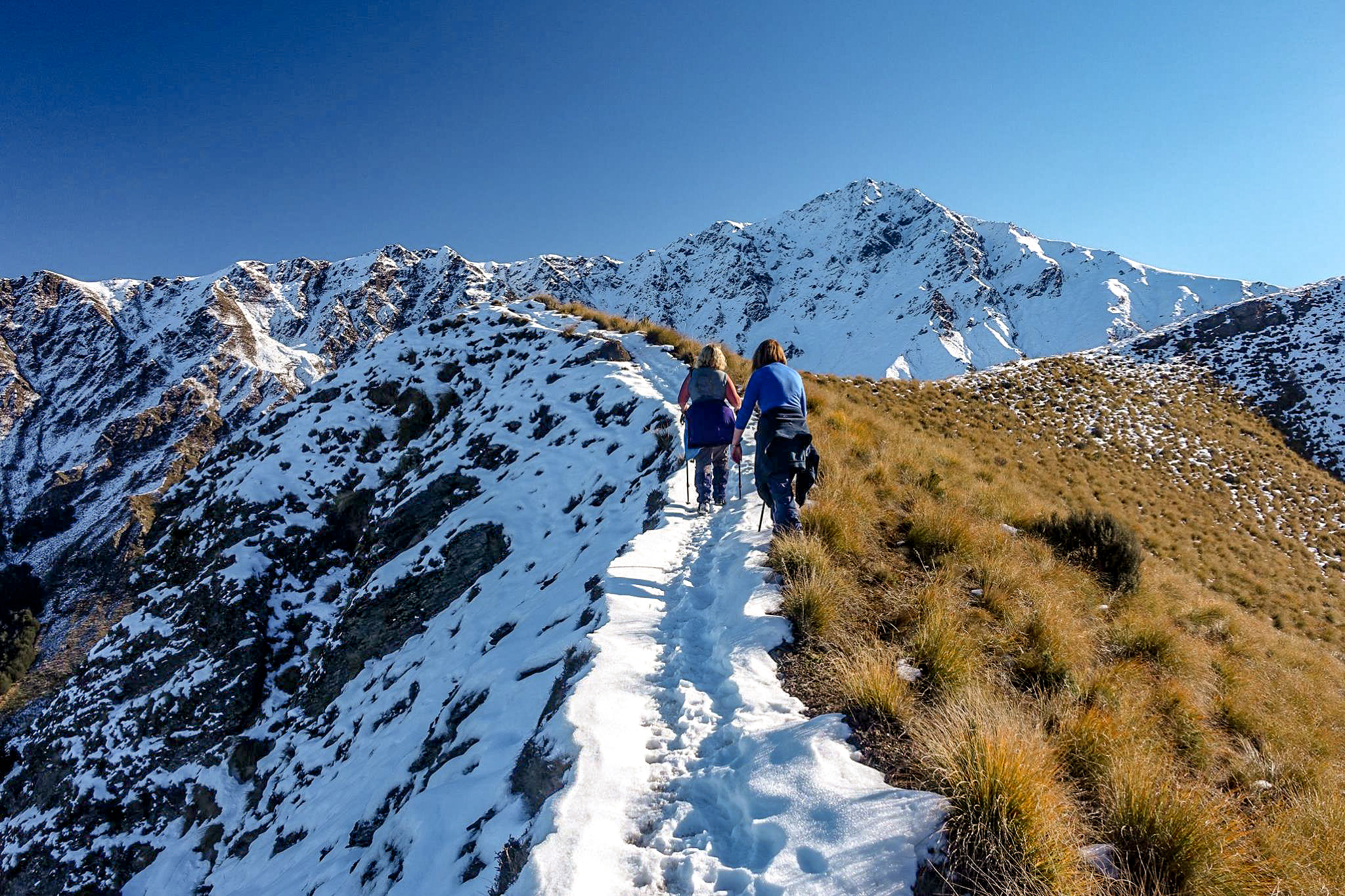 Two female hikers climbing up a snowy ridge with Ben Lomond in the background